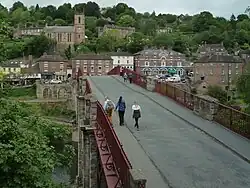 Pedestrians walking over a bridge with red-brown hand rails