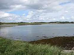 The white farmhouse on the raised beach stands adjacent to the Millin Bay Cairn