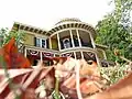 House with a round protruding porch with white columns and red-white-blue banners; red leaves in foreground