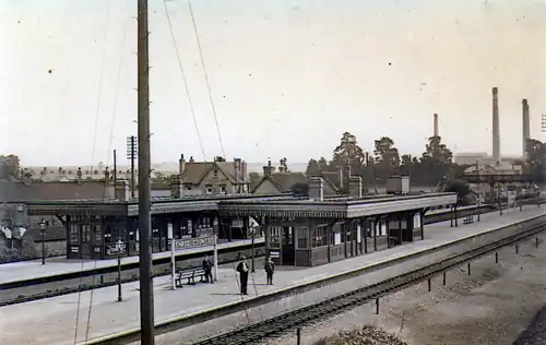 A station with two island platforms and four tracks as photographed in black and white from higher ground a short distance away. A telegraph pole obstructs the camera's view, and a sign on the platform says "THREE COUNTIES". There are also platform buildings and people standing on the right-hand platform.