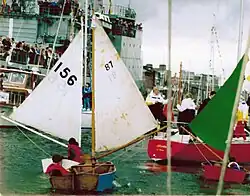 Three small wooden sailing boats behind a yacht sail up a river.