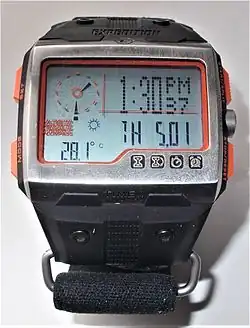 The Timex Expedition WS4 in time display mode. The temperature displays 28.1 degrees Celsius while the sun icon indicates the barometric pressure trend is positive, forecasting improving weather ahead. The digital time is also displayed through an LCD watch with analogue hands located on the upper left corner of the dashboard.