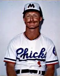 A man wearing a white baseball uniform and blue cap with a white "M".