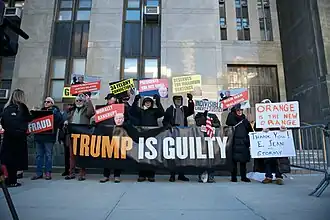 A small group of people hold up a banner reading "Trump is guilty" among other anti-Trump signs.