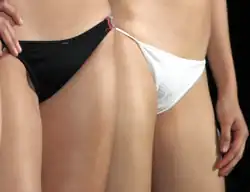 Two women; one is wearing black conventional bikini underwear and the other is wearing white string bikini underwear.