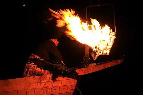 Boat, man, cormorant and a fire at the end of the boat at night.