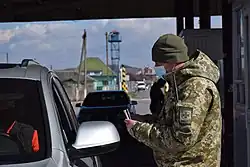 Ukrainian civilians in a car wait at the border checkpoint with Hungary with a soldier taking registration