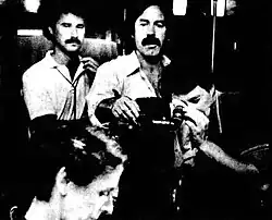 Director Don Gronquist viewing Janet Penner through a camera lens as two other men look on.