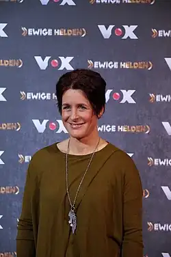 A woman stands in front of a background and smiles for photographs.