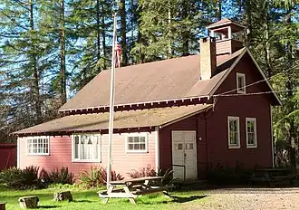 Photograph of the Venersborg School, a small, red, one-and-one-half story gabled building with a cupola and bell, in a forested setting