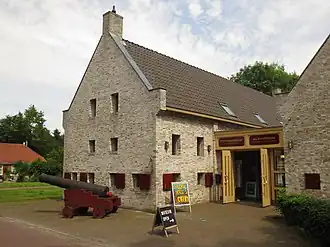 Light yellow brick building with dark red shutters and with a canon in front of it