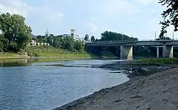A middle-sized river with sandy and grassy banks flows under a bridge.