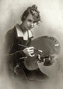 formal, hip height portrait of young woman with long hair pulled up into a knot, wearing long sleeved dark velvet dress with light collar, holding a paintbrush and palette