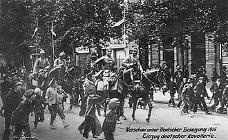A black and white image of soldiers on horseback with children watching on either side of them