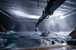 Behind-the-scenes picture of filming taking place with actors on a raft in a large water tank