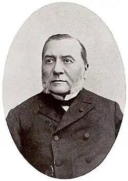 A middle-aged man with white mutton chops wearing a black peacoat