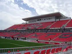 A view of a soccer stadium's uncovered stand with the letters "TORONTO" spelled in contrasting colored seats under a press box.