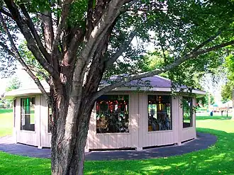 A shelter building containing a historic carousel with a tree in the foreground