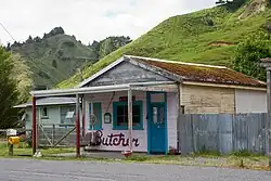 A picture of derelict butcher shop with forested, hilly environs