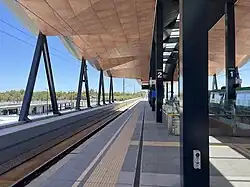 An elevated train station platform viewed from the platform, with shelter overhead