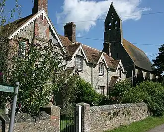 A row of cottages, partially obscured by vegetation. In the background is the bell tower of a much large building.