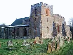 A stone church seen from the northwest with a squat tower in the foreground, with the north aisle to the left and the west end of the nave to the right