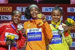 Three woman are on the podium holding their medals. Hassan is in the middle holding a gold medal.