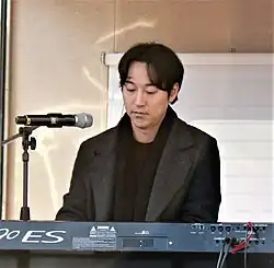Yiruma looks down as he plays the piano.