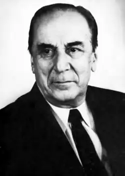 A balding man with dark hair in a black suit and tie