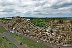 A historic unpainted roller coaster with trees and a bay in the background