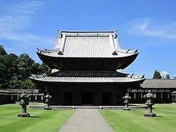 Wooden building with a metal plate covered roof and an enclosing pent roof giving it the appearance of a two-storied structure.